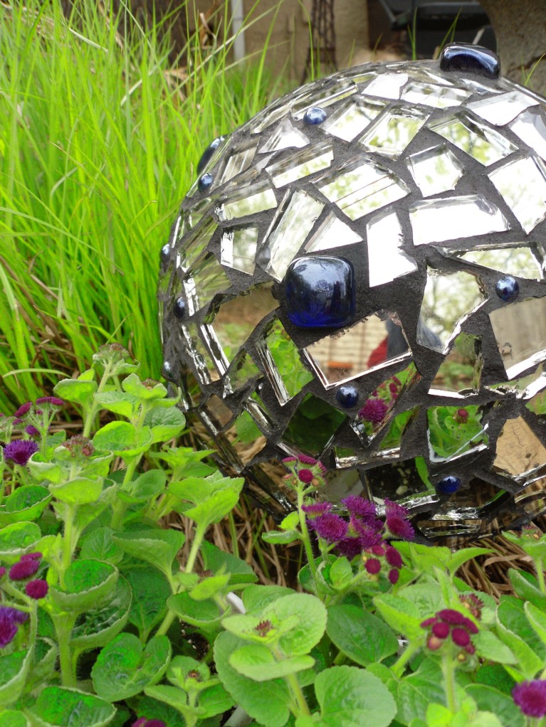 A bowling ball makes a great base for a garden mosaic gazing ball. Broken mirror pieces and blue marbles glued-on and grouted do the trick. Leave a hole open to prop the ball on a dowell or stake in the garden.